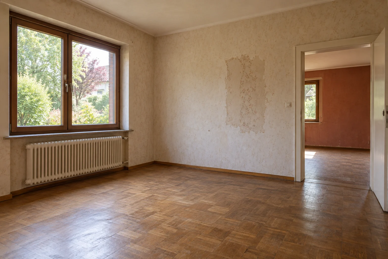 Leerer älterer Wohnraum mit abgenutztem Parkett, älterem Heizkörper und renovierungsbedürftigen Wandflächen.